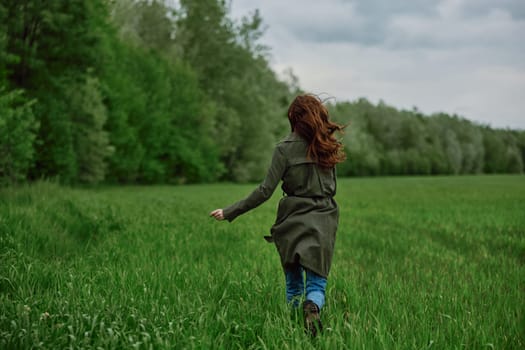 a woman in a long raincoat runs across a field in tall green grass in cloudy weather in spring. High quality photo