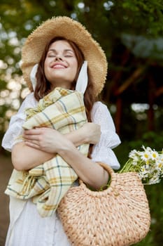 portrait of a beautiful, happily smiling woman in a light dress, a plaid in her hands and with a wicker hat enjoys outdoor recreation. High quality photo