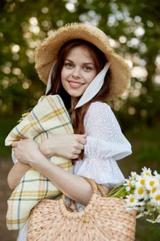 portrait of a beautiful, happily smiling woman in a light dress, a plaid in her hands and with a wicker hat enjoys outdoor recreation. High quality photo