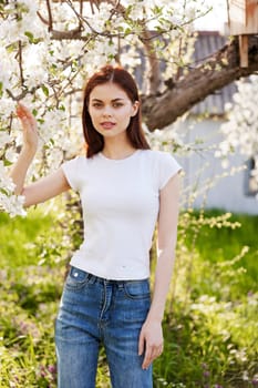 a pretty woman in casual clothes stands near a flowering tree in tall grass. High quality photo