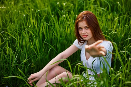 the girl sits in the tall grass and extends her hand for help. High quality photo