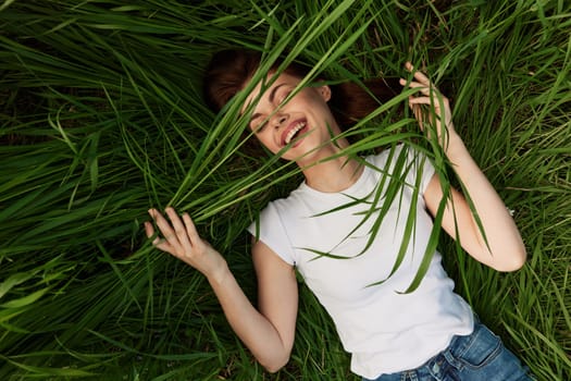 happy woman lying in tall grass holding leaves with her hands. High quality photo