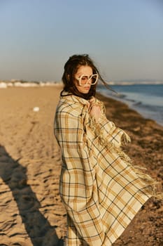 a beautiful woman wrapped in a plaid stands on the seashore against the backdrop of sunset. High quality photo