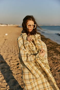 a beautiful woman wrapped in a plaid stands on the seashore against the backdrop of sunset. High quality photo