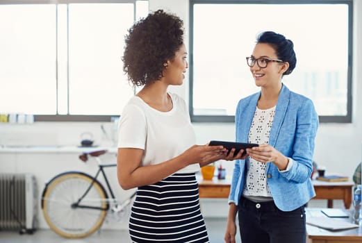 Sharing technology in the office. two young designers talking together over a digital tablet in an office