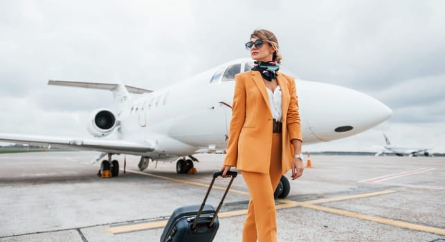 Cloudy weather. Passenger woman that is in yellow clothes, sunglasses and with luggage.