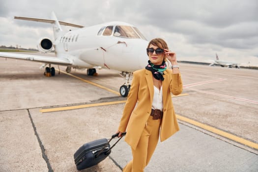 Cloudy weather. Passenger woman that is in yellow clothes, sunglasses and with luggage.