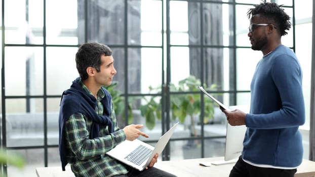 Young businessman holding laptop while discussing new project with african american colleague