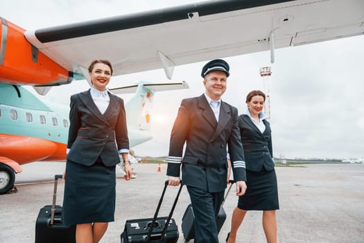 With luggage. Aircraft crew in work uniform is together outdoors near plane.