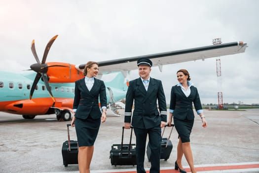 With luggage. Aircraft crew in work uniform is together outdoors near plane.