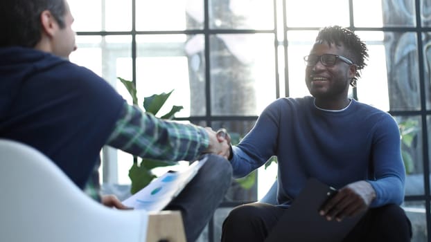 a black man with a folder in his hands shakes hands with an interlocutor in the lobby of the office