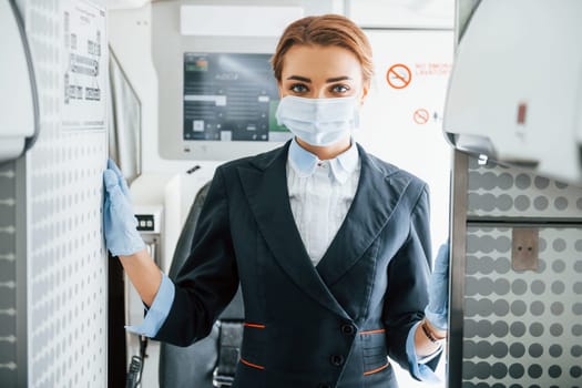In mask. Young stewardess on the work in the passanger airplane.