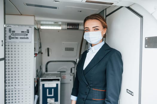 In protective gloves and mask. Young stewardess on the work in the passanger airplane.