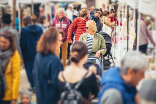 Mother waling and pushing his infant baby boy child in stroller in crowd of unrecognizable people wisiting sunday flea market in Malaga, Spain