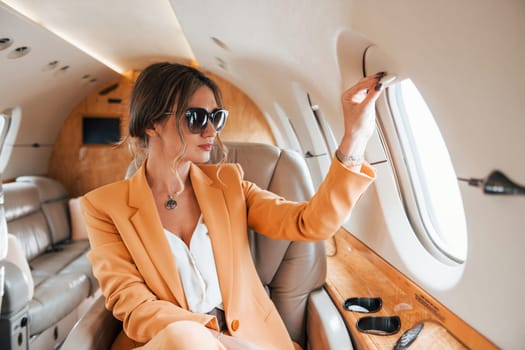 In sunglasses. Young passenger woman in yellow clothes is flying in the plane.