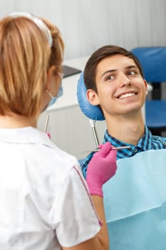 Handsome young man is having dental check up in dental office. Dentist is examining a patient with dental tools