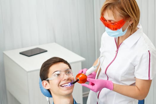 Beautiful woman dentist treating teeth in dental office. Doctor wearing glasses, mask, white uniform and pink gloves. Dentistry