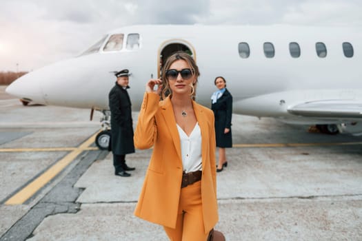 A young woman in yellow clothes is accompanied by an airline workers.