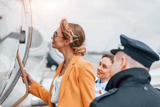 A young woman in yellow clothes is accompanied by an airline workers.