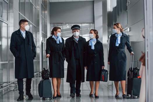 Aircraft crew in work uniform is together outdoors in the airport.