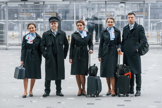Aircraft crew in work uniform is together outdoors in the airport.