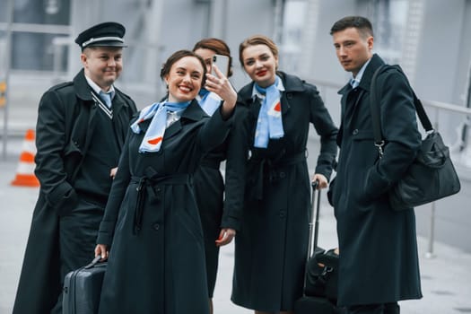 Aircraft crew in work uniform is together outdoors in the airport.