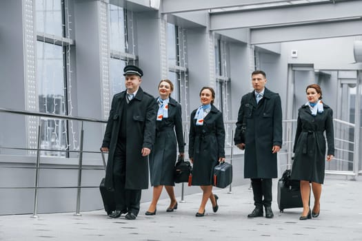 Aircraft crew in work uniform is together outdoors in the airport.