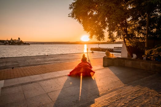 Sunrise red dress. A woman in a long red dress against the backdrop of sunrise, bright golden light of the sun's rays. The concept of femininity, harmony