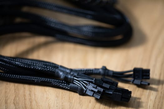 Black modular power cables for a computer lying on a brown wooden top. Close-up of black computer cables. Blurred background.