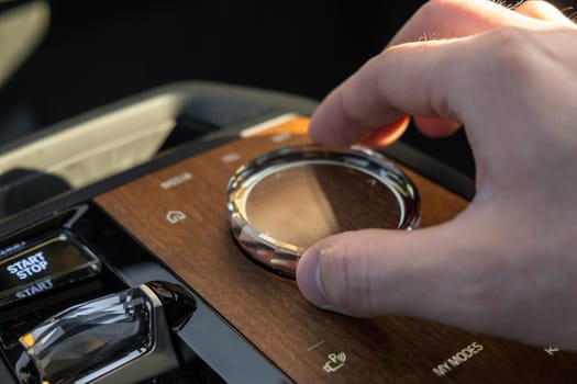 PRAGUE , CZECH REPUBLIC - MARCH 10 2022: Man uses multimedia system control in luxury car BMW IX. Hand of driver adjusting mode in automobile with stylish interior close view