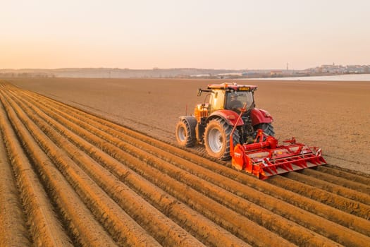 PRAGUE , CZECH REPUBLIC - MARCH 18 2022: Heavy tractor uses plow to make beds for planting potatoes in agricultural field. Powerful machine operates at farm on sunny day aerial view