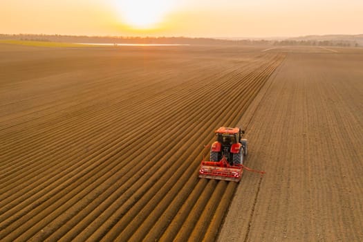 Red tractor working in agricultural field at sunset to avoid a food crisis.