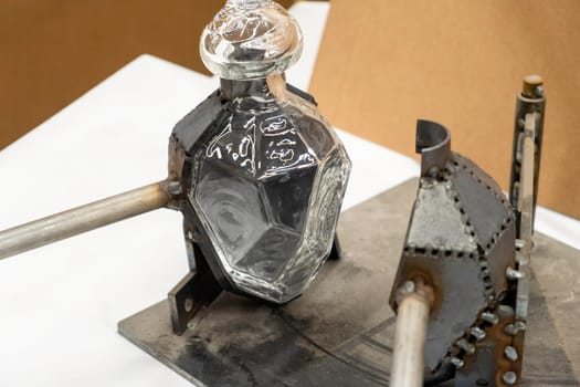 Stylish glass bottle in open metal form on workbench in light workshop at traditional glassblowing plant extreme close view