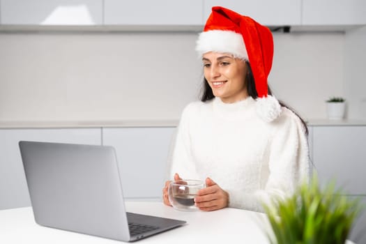 Happy woman with a coffee cup has a meeting online before Christmas. Freelance girl working at home office.