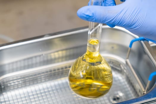 Scientist in blue rubber puts a yellow solution in the flask for dissolving or extraction into ultrasound bath. Urea analysis. Clinical, toxicological and forensic analysis.