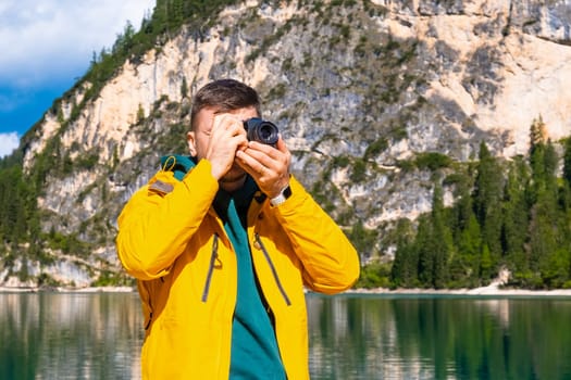 Portrait of the photographer covering her face with the camera on the background of Lake Braies and the Dolomites