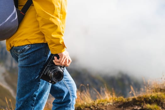 Legs of hiking woman standing and holding a retro camera on the peak of the mountain covered by clouds. Travel concept.