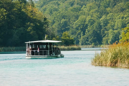 Excursion ship stands near the pier against green forest. Touristic attraction in natural park reserve on Plitvice lakes