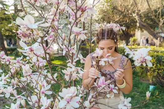 Magnolia flowers, a girl smells a blooming magnolia in the park in the sun, enjoys her vacation