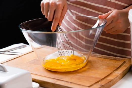 Close up of a womans hands whipping eggs for making dough on the wooden desk in the kitchen. Homemade cooking.