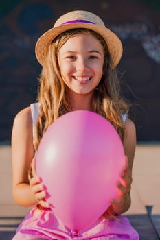 Portrait of a girl in a hat with a pink balloon. She is dressed in pink clothes and her hair is long and loose