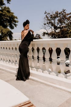 Stylish woman in the city. Fashion photo of a beautiful model in an elegant black dress posing against the backdrop of a building on a city street.