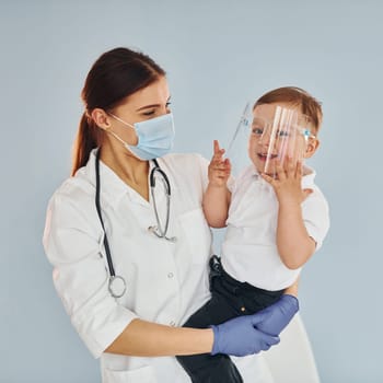 Young nurse in white coat and with stethoscope holds little boy in hands.