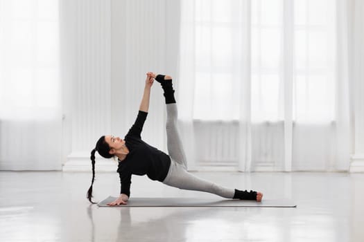 Young woman instructor doing vertical splits during yoga class in cozy living room. The concept of energy, strength and flexibility, as well as to get rid of tension, negativity and stress.