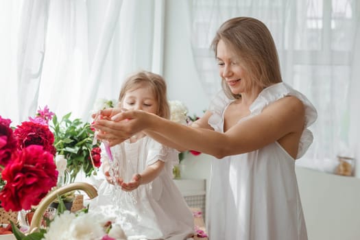 A little blonde girl with her mom on a kitchen countertop decorated with peonies. The concept of the relationship between mother and daughter. Spring atmosphere