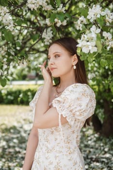 An attractive long-haired woman walks in the spring in the park of blooming apple trees. Spring portrait of a woman