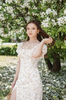 An attractive long-haired woman walks in the spring in the park of blooming apple trees. Spring portrait of a woman