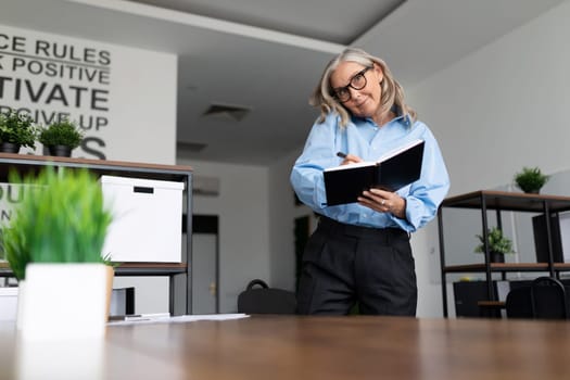 mature adult female accountant with gray hair holding a notepad in her hands in the office.