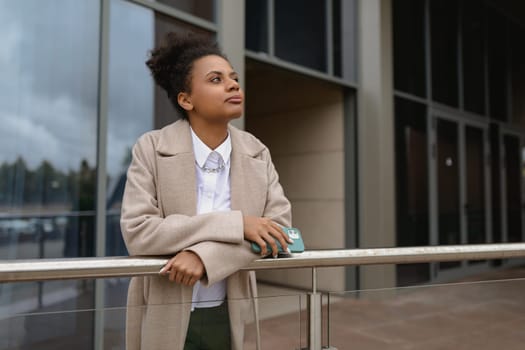 American young woman designer stands thoughtfully in front of a glass business center.