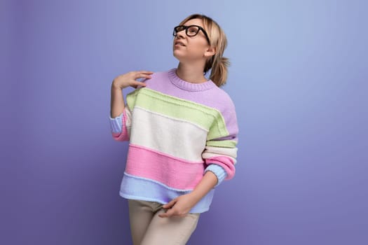 cute attractive blond woman in a striped sweater with eyeglasses on a purple background with copy space.